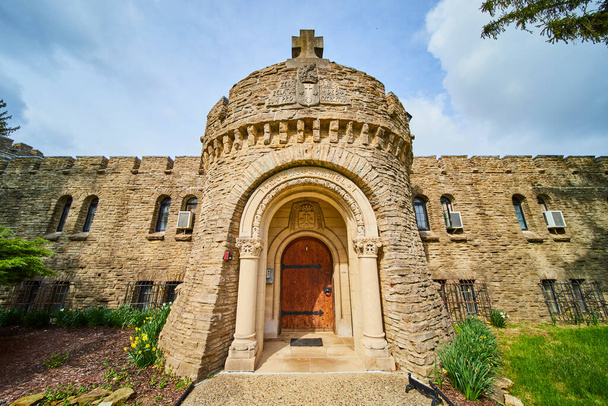 Biskup Simon Brute College středověká kamenná věž pod částečně zamračenou indiánskou oblohou, s křížovými a zdobenými dřevěnými dveřmi. - Fotografie, Obrázek