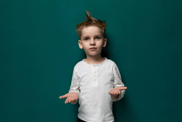 Uma criança do sexo masculino é mostrada em pé na frente de uma parede verde vibrante, olhando diretamente para o espectador. Ele parece curioso e engajado, com uma expressão neutra. - Foto, Imagem