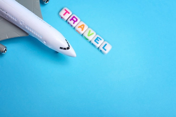 Passenger plane on a blue background with the inscription travel next to it. Travel concept - Photo, Image