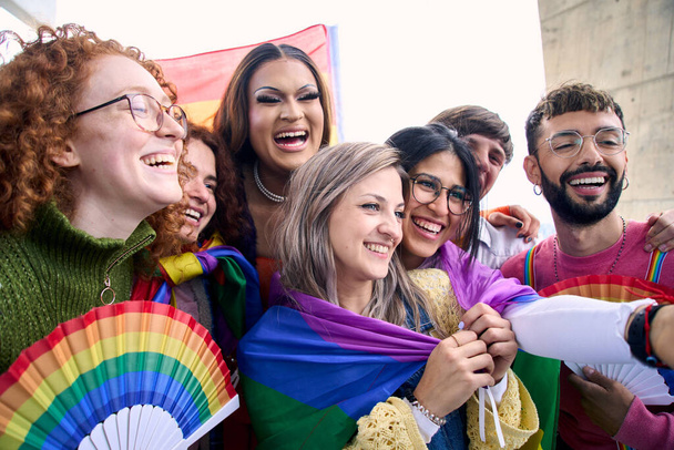 Ομάδα από χαρούμενους νέους φίλους που βγάζουν μια selfie φωτογραφία απολαμβάνοντας μαζί την ημέρα gay υπερηφάνειας. Χαρούμενοι ΛΟΑΤ άνθρωποι συγκεντρώθηκαν αγκαλιασμένοι και χαμογελαστοί στην ύπαιθρο. Σχέσεις της γενιάς z - Φωτογραφία, εικόνα