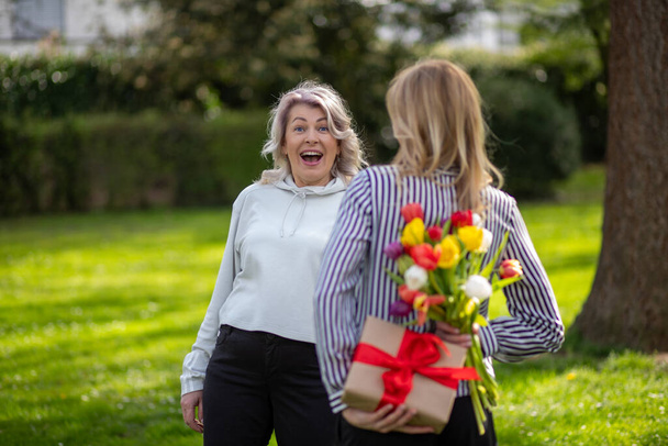 Daughter surprises mother with hidden gift and flowers behind back - Photo, Image