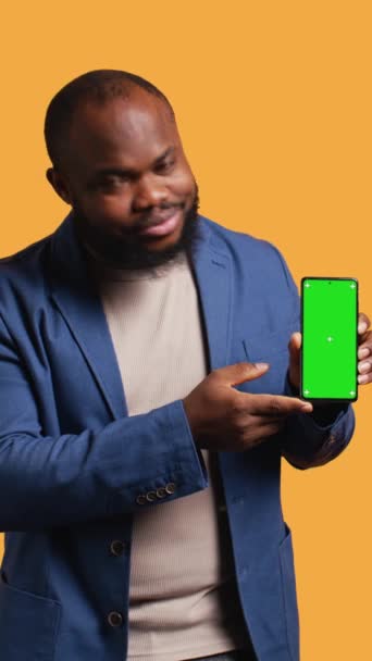 Dikey video Mutlu Afro-Amerikan adam elinde yeşil ekran telefon, tavsiye yapıyor. Neşeli BIPOC çalışanı sunar, tasvir cihazı, onay işareti, stüdyo arka planı, kamera B - Video, Çekim