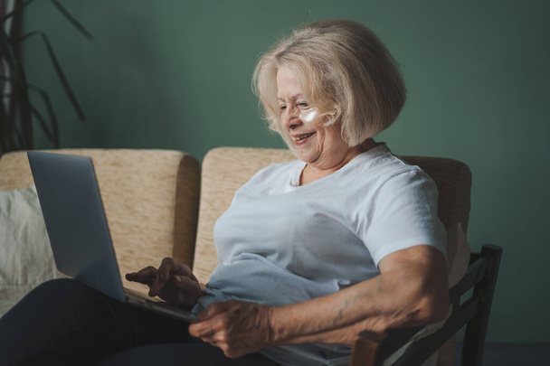 Laptop ekranına bakıp internetten haber okuyan olgun, emekli bir kadın. Büyükanne sosyal ağda iletişim kuruyor. Yaşlılar ve modern teknoloji. - Fotoğraf, Görsel