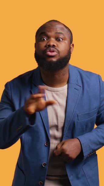 Függőleges videó Annoyed afro-amerikai férfi csinál shushing kéz gesztikulál, irritálja a zaj, amelynek negatív hangulata. Személy üzembe ujját az ajkak, csinál csendes jel gesztus, stúdió háttér, kamera - Felvétel, videó