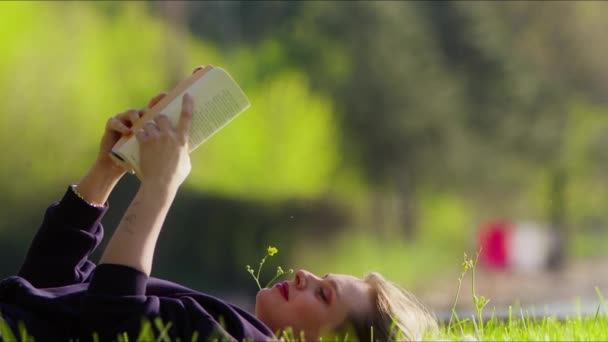 Jeune femme lit livre sur l'herbe dans la nature - Séquence, vidéo