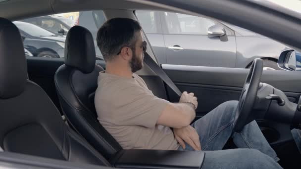 Biztonsági első, mint egy fiatal felnőtt férfi kapcsolja be a biztonsági övét vezetés előtt. A jelenet egy biztonságtudatos pillanatot rögzít egy kortárs járműben.. - Felvétel, videó