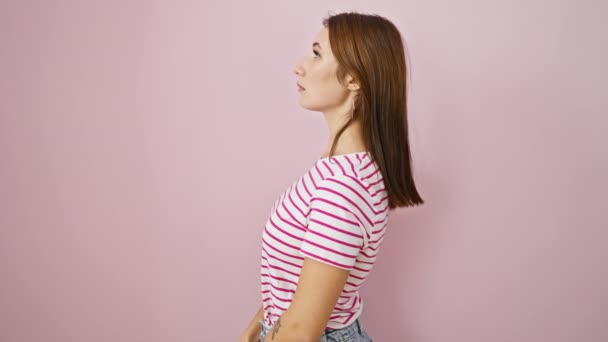 Giovane ragazza bruna allegra colta in una posa naturale e sicura, guardando da una parte con un sorriso. indossando una t-shirt a righe su uno sfondo rosa isolato. - Filmati, video