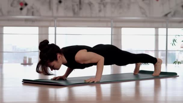Young athletic girl training yoga at fitness studio, standing in plank. Female performing Urdhva Chaturanga dandasana poses. Flexible female practicing yoga in studio. Fitness concept - Footage, Video