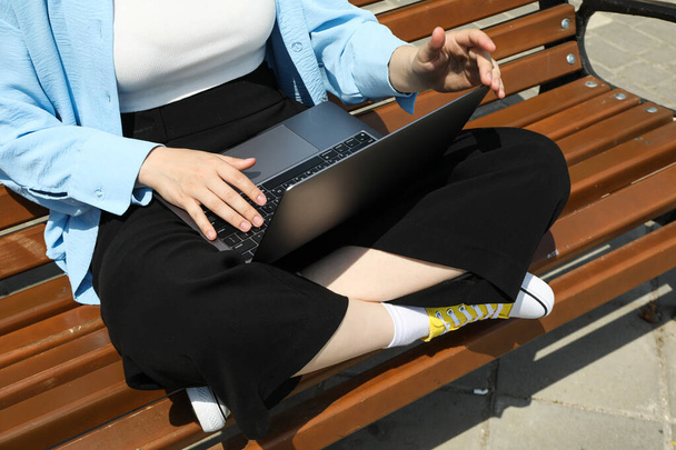 A lány laptopon dolgozik, miközben egy padon ül. - Fotó, kép