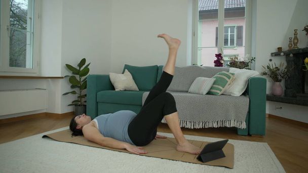 Femme faisant de l'exercice à la maison allongée sur le plancher du salon levant la jambe pendant la grossesse du troisième trimestre. Grossesse 30s dame séance d'entraînement pendant l'exercice prénatal - Photo, image