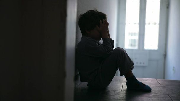 Bambino in crisi familiare, seduto solitario nel corridoio mal illuminato, volto coperto di mani per esprimere dolore e dolore profondi - Foto, immagini