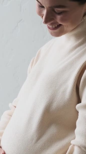 Detailní portrét pozitivní těhotné bělošky hladící břicho doma. Budoucí rodičovství a mateřství, koncept náklonnosti. Svislé video. - Záběry, video