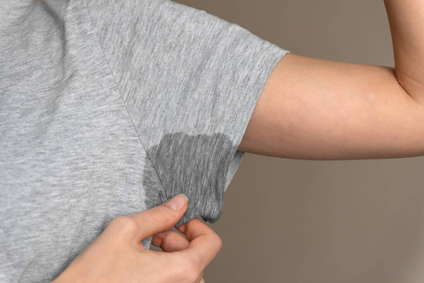 Close-up of a young woman shows a wet armpit on a gray T-shirt. Concept of health, sports - Photo, Image
