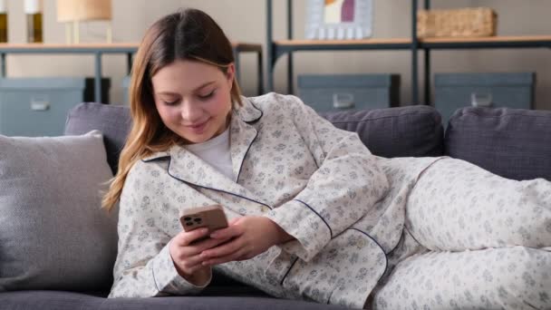 Mutlu Kafkasyalı kadın, evde oturma odasında kanepeye uzanmış, telefonla internetten sosyal medyaya mesaj atıyor. Uzaktan iletişim, internet eğlence kavramı. - Video, Çekim