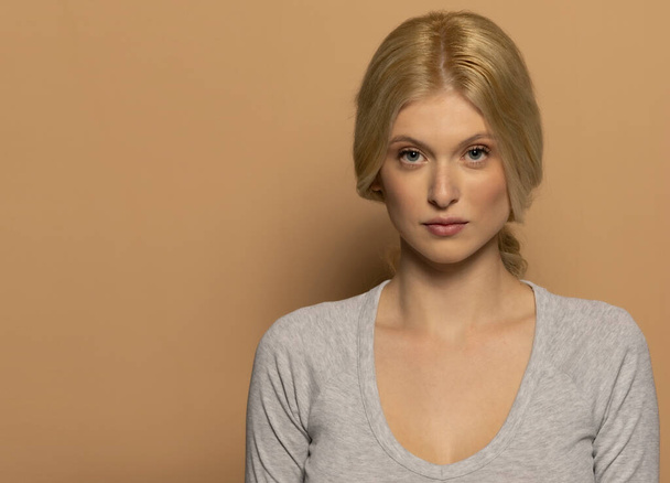 Portrait de beauté de jeune mannequin avec de longs cheveux blonds attachés sur fond studio beige - Photo, image