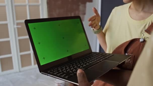 Over schouder beelden van gezichtsloze paar overweegt home renovatie proces en het ontwerp van ideeën op zoek naar groene chroma key screen op laptop in onafgewerkte kamer - Video