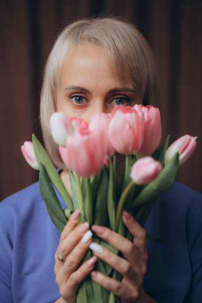Egy szőke hajú, kék inges nő egy csomó tulipánt tart a kezében. - Fotó, kép