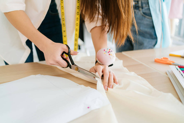 Zamknij rękę krawca lub projektanta mody cięcia tkaniny z nożyczkami do tworzenia wzoru ubrania. Projektant mody krawiec lub kanalizacja w warsztacie pracy na nowe ubrania kolekcji. - Zdjęcie, obraz