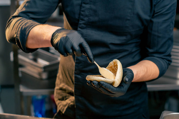close-up van een chef-kok in zwarte handschoenen met verschillende sauzen op een broodje met een lepel - Foto, afbeelding