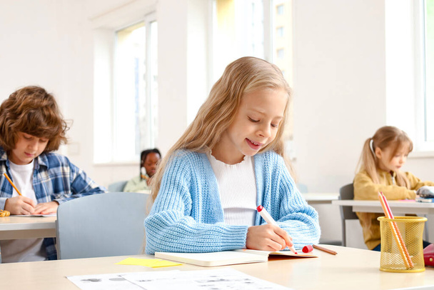 Χαμογελώντας κορίτσι του σχολείου κρατώντας σημειώσεις στο σημειωματάριο, ενώ κάθεται στην τάξη. Εκπαιδευτική ιδέα. Πίσω στο σχολείο. - Φωτογραφία, εικόνα