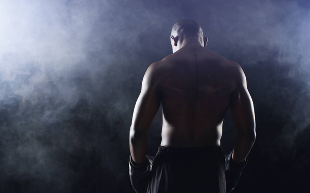 Man, boxer and back of fighter athlete on black background in studio with smoke mist, competition or muscle. Male person, gloves and rear view for sports exercise with endurance, training or serious. - Photo, Image