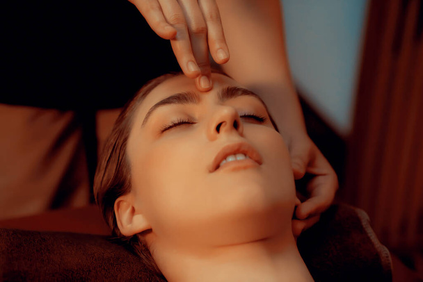 Femme caucasienne profiter relaxant anti-stress massage de la tête et choyer beauté faciale loisirs de la peau dans la bougie chaude éclairage spa salon ambiant dans un complexe de luxe ou un hôtel. Tranquillité - Photo, image