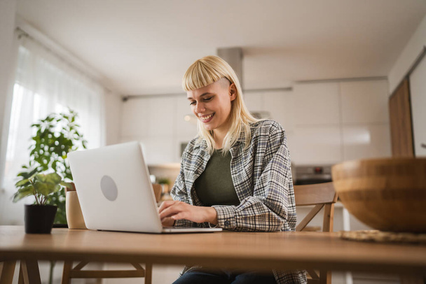 Nuori valkoihoinen blondi nainen työskentelee kannettavan tietokoneen kotoa onnellinen positiivinen - Valokuva, kuva