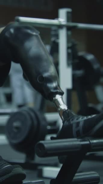 Tiro vertical de atleta com prótese em trens de perna na máquina de treino no centro de fitness moderno. Adulto desportivo homem com deficiência física faz treinamento de força usando esportes profissionais ginásio - Filmagem, Vídeo