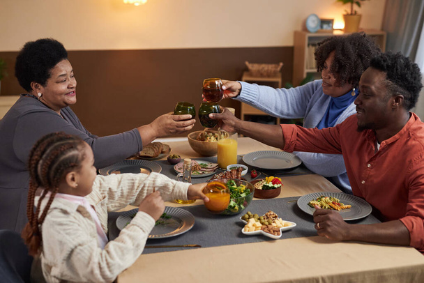 Muotokuva kolmen sukupolven Afrikkalainen amerikkalainen perhe nauttii illallista yhdessä kodikas koti ja clinking lasit paahtoleipää yli taulukon kopiotilaa - Valokuva, kuva