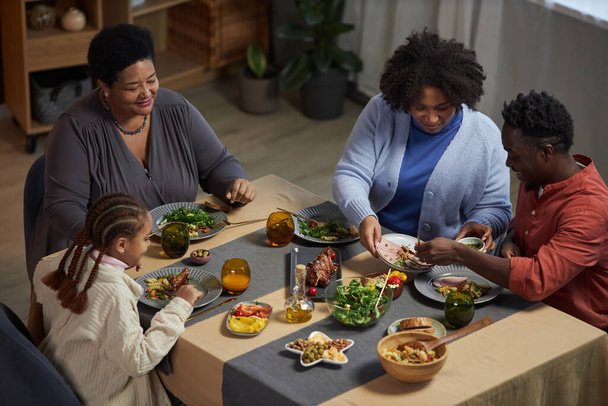 Υψηλής γωνίας πορτρέτο της οικογένειας τριών γενεών απολαμβάνοντας το δείπνο μαζί κάθεται στο τραπέζι στο σπίτι και μοιράζονται τα τρόφιμα - Φωτογραφία, εικόνα