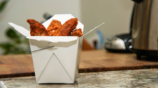 Une boîte de lanières de poulet frit brun doré est placée sur un comptoir de cuisine, avec un fond flou - Photo, image