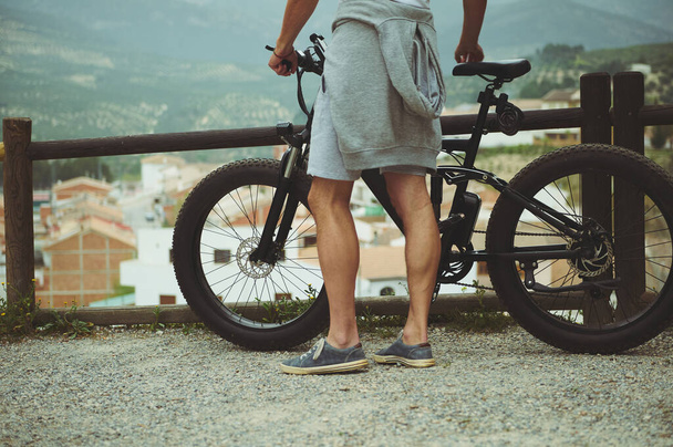 バックから電池式自転車の近くに立っている若いアクティブな男性のサイクリストに近い眺め,美しい山々を賞賛し,自然の中で乗って楽しんでいます. 人々よ。 自由とは。 エコトランスポート - 写真・画像