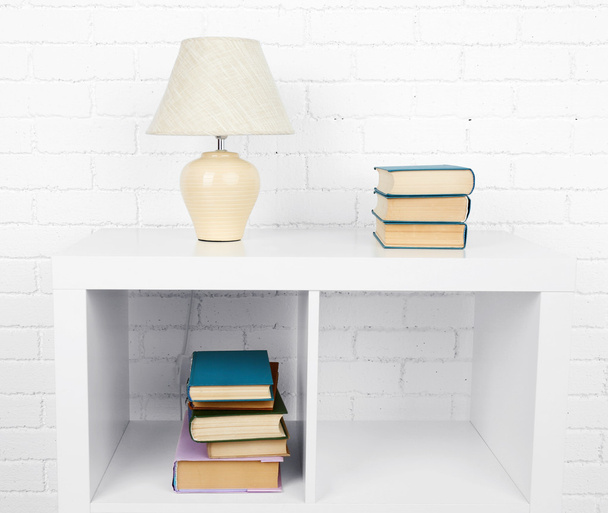 Wooden shelf with books and lamp on brick wall background - Foto, imagen