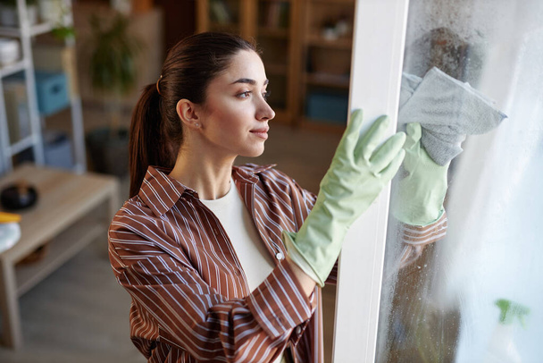 Vista laterale ritratto di giovane donna che pulisce le finestre a casa e indossa guanti di gomma copiare spazio - Foto, immagini