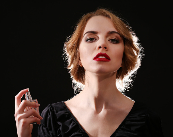 Beautiful young woman with perfume bottle on black background - 写真・画像