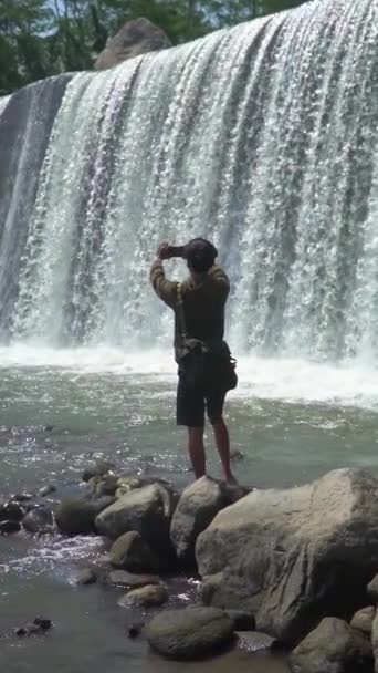 Азиатский человек отдыхает в одиночку на Сабо плотины искусственного водопада, который имеет 6 уровней. Вид сзади человека наслаждается прекрасной панорамой плотины Сабо, которая имеет 6 уровней воды - Кадры, видео