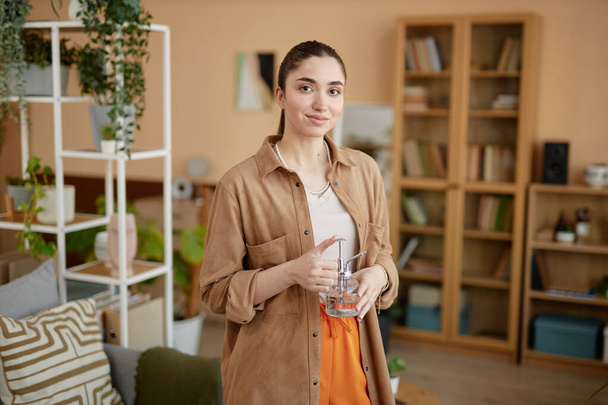 Портрет молодої жінки, що тримає скляну посудину і посміхається на камеру вдома копіювати простір - Фото, зображення