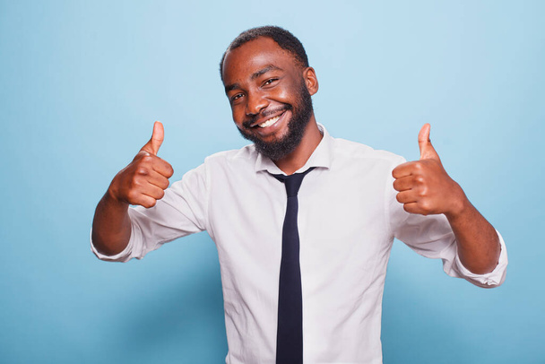 Πορτρέτο ενός Αφροαμερικανού που δείχνει τους αντίχειρες του μπροστά στην κάμερα. Θετικό μαύρο άτομο που δίνει σαν και την έγκριση, αισθάνεται χαρούμενος και ενθουσιασμένος ενώ διαφημίζει θετικότητα. - Φωτογραφία, εικόνα