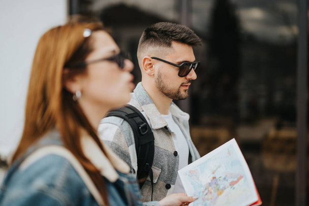 Een jonge man en vrouw, toeristen, onderzoeken een kaart tijdens het verkennen van een stedelijke omgeving onder zonnige omstandigheden, met een moment van avontuur tijdens hun reis. - Foto, afbeelding
