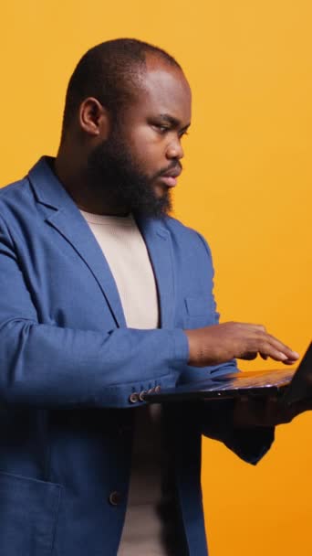 Κάθετη βίντεο Αφρικής Αμερικανός άνθρωπος χρησιμοποιώντας φορητό υπολογιστή για να κάνει επιχειρηματικές εργασίες για την εταιρεία, απομονώνονται σε στούντιο φόντο. Υπάλληλος γραφείου που εκτελεί κατάρτιση του προϋπολογισμού, πρόβλεψη, και τη χρηματοοικονομική ανάλυση για - Πλάνα, βίντεο