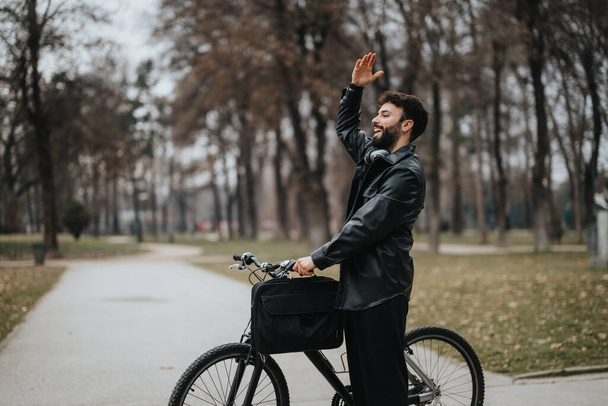 Stylish male entrepreneur working remotely while enjoying the outdoors in an urban park, waving and greeting. - Photo, Image