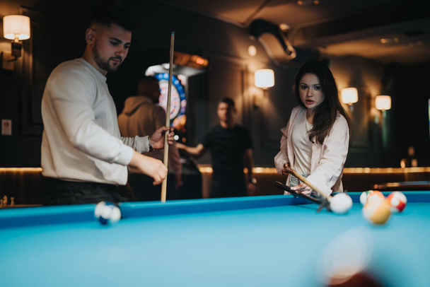 Group of young adults having fun playing billiards together in a relaxed, recreational setting at night. - Photo, Image