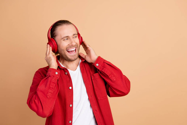 Portrait of nice young man headphones empty space wear red shirt isolated on beige color background. - Foto, Bild