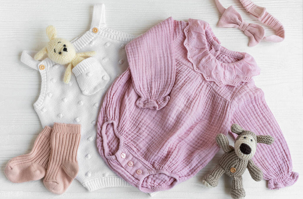 新生児のためのピンクの服とアクセサリーのセット. ウサギや犬,ロマー,ソックス,ハンドバンドを白い木の背景に編まれたおもちゃ. ベビーシャワーコンセプト。 フラットレイ,トップビュー - 写真・画像