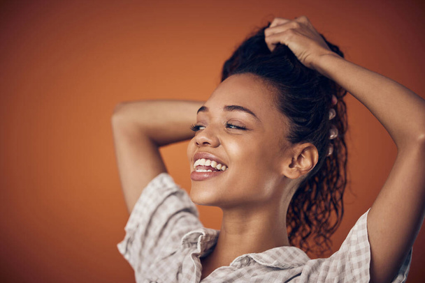 Washing, smile and woman with wet hair in studio with cosmetics, shampoo or treatment on orange background. Haircare, model and scalp detox with growth, texture or cleaning, serum or gel application. - Photo, Image