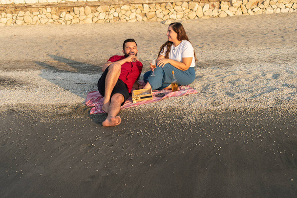 Couple savourant du vin et conversation sur une plage au coucher du soleil. - Photo, image