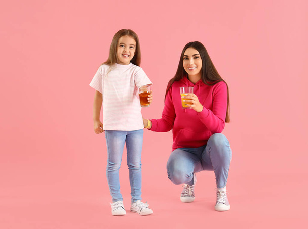Маленька дівчинка з матір'ю і склянки соку на рожевому фоні - Фото, зображення