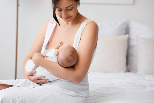 gelukkig moeder borstvoeding haar weinig schattig baby in slaapkamer - Foto, afbeelding