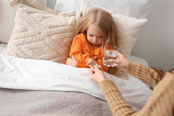 Άρρωστο κοριτσάκι που παίρνει χάπια από τη μητέρα της στην κρεβατοκάμαρα. - Φωτογραφία, εικόνα