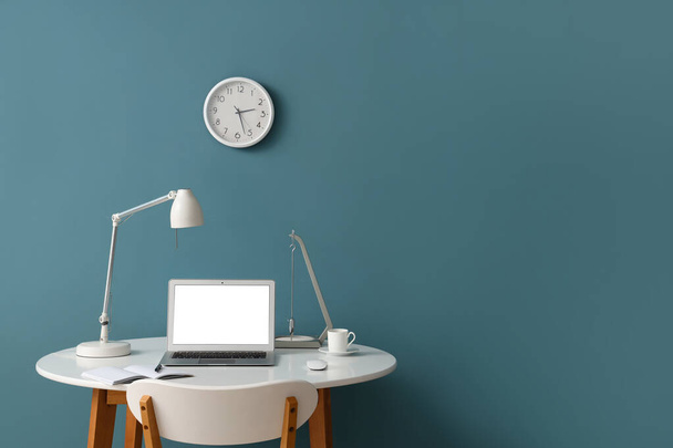 Κομψό χώρο εργασίας με σύγχρονο φορητό υπολογιστή, σημειωματάριο και φλιτζάνι καφέ κοντά στον τοίχο χρώμα - Φωτογραφία, εικόνα